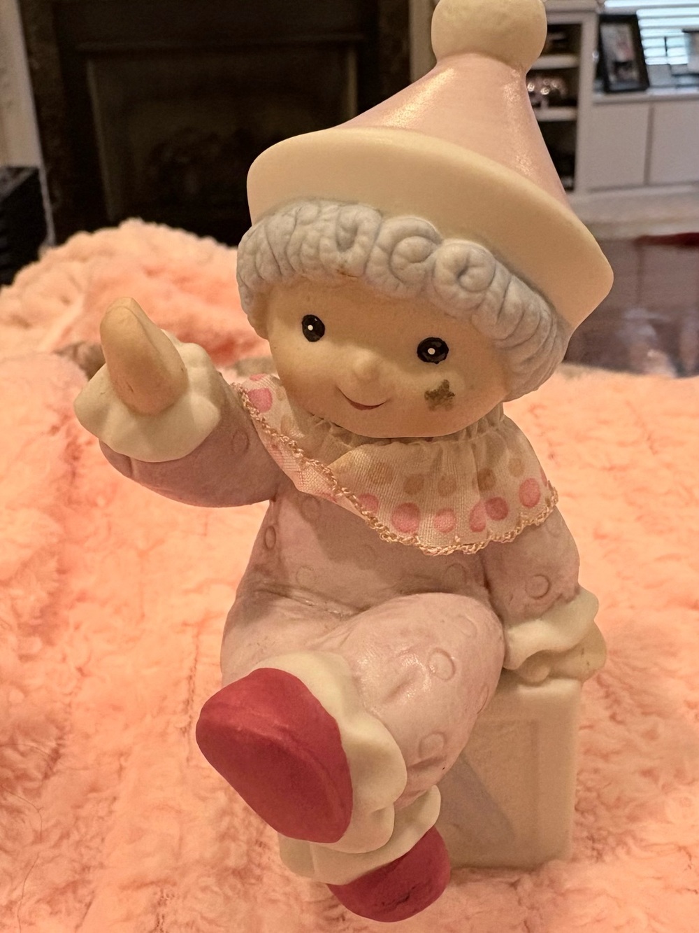 Hand -painted pastel pink-clad baby clown wearing a textured hat.